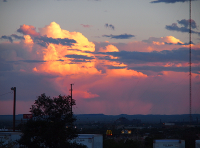 [A large white topped cloud with pink/purple bottom is behind some horizontal, skinny slate blue clouds.]